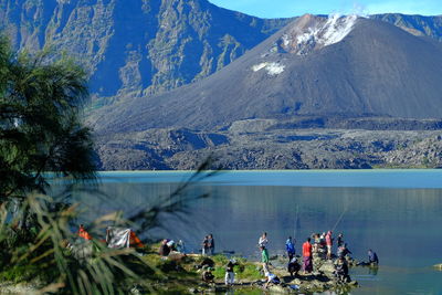 People at lakeshore against mountains