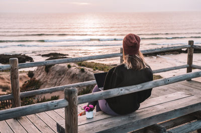 Rear view of woman sitting on railing against sea