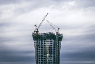 Low angle view of crane at construction site against sky