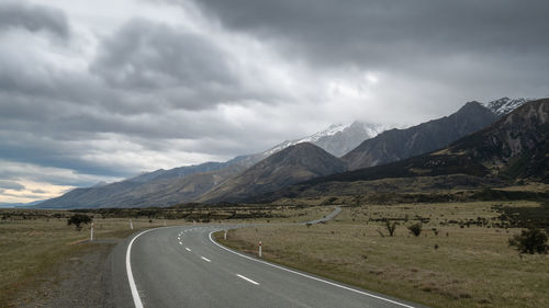 Road leading towards mountains, with cloudy sky.  aoraki mt cook national park in new zealand