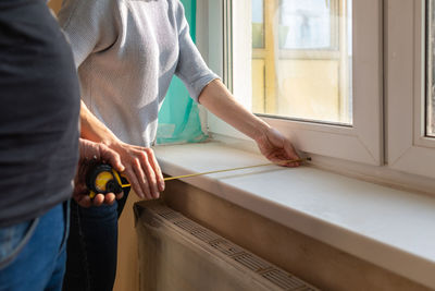 Young couple moving in new apartmen. people measure size of window sill with a tape measure. concept 