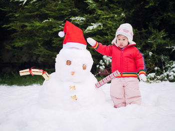 Cute toddler girl standing by snowman during winter