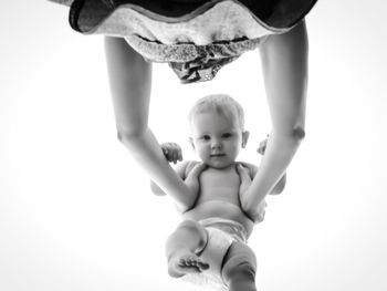 Directly below view of mother lifting baby girl against white background