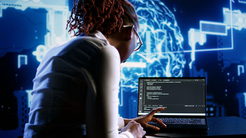 Rear view of woman using laptop at night