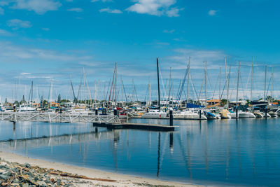 Sailboats moored at harbor against blue sky