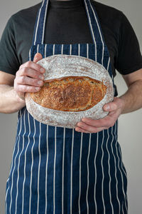 Close-up at bakers hands holding a loaf of organic sourdough bread in front of him.