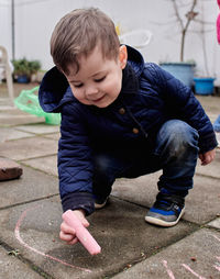 Smiling boy is drawing with chalk on the ground