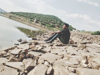Young man on rocks against sky