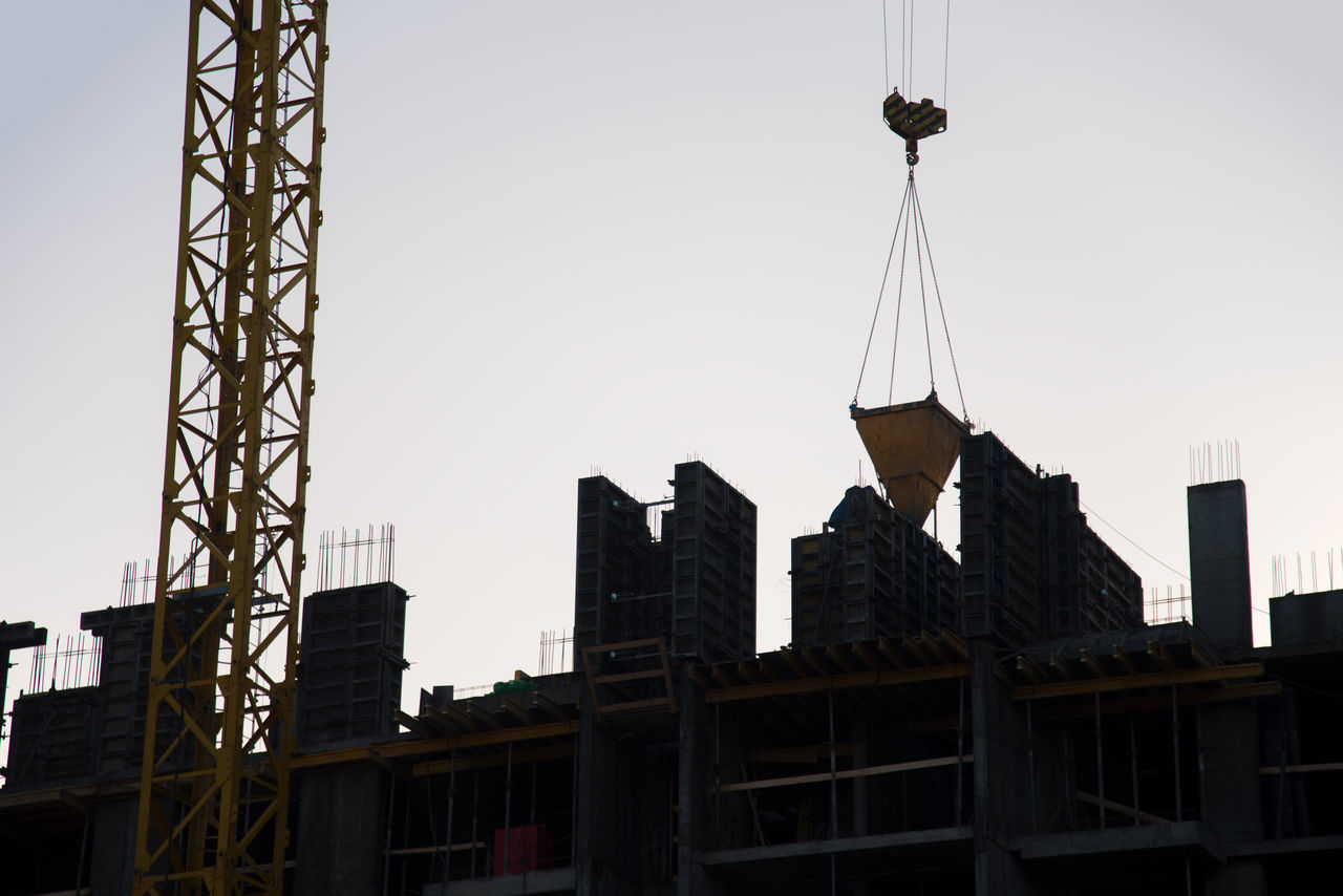 LOW ANGLE VIEW OF CRANE BY BUILDING AGAINST CLEAR SKY