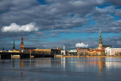 View of city at waterfront against cloudy sky