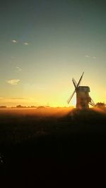 Silhouette of windmill on field against sky during sunset