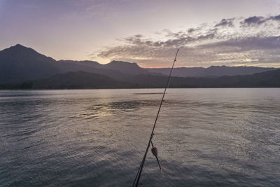 Fishing rod against river and sky at dusk