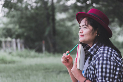 Thoughtful woman holding pen and book in park