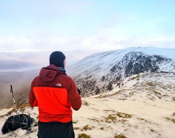 Rear view of man standing on snowcapped mountain