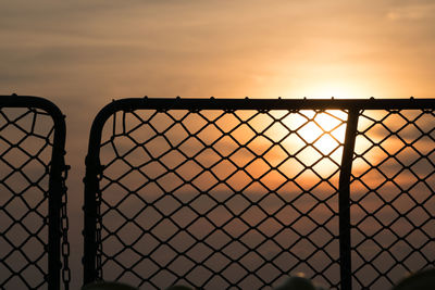 Close-up of chainlink fence against sky during sunset