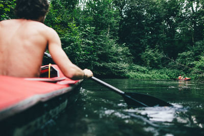 Shirtless man kayaking in lake at forest