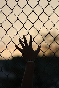 Silhouette man standing on chainlink fence