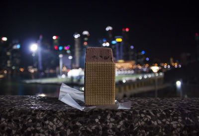 Close-up of ice cream sandwich, illuminated city by river against buildings at night