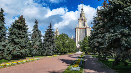 Road amidst trees and buildings against sky