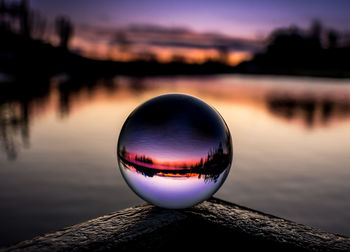 Close-up of crystal ball on wooden post at lake during sunset