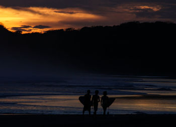 Silhouette men holding surfboards while standing at beach during sunset