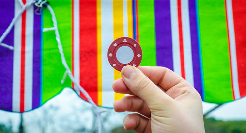 Cropped image of person showing gambling chip with striped drape in background