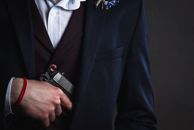 Midsection of man holding handgun against black background