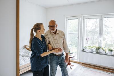 Female nurse supporting elderly male walking at nursing home