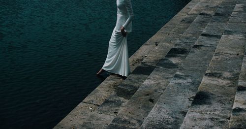 Low section of woman wearing dress walking down steps towards river