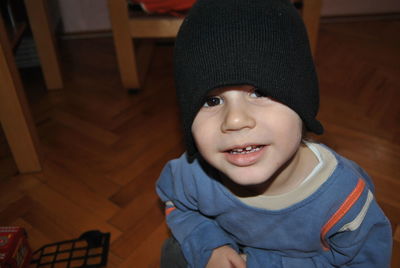 Portrait of boy wearing knit hat while crouching on hardwood floor