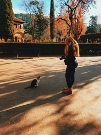 Side view of woman with camera standing by cat in park