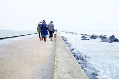 People walking on pier in sea at hook of holland against sky