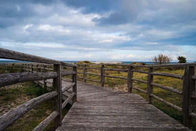 Wooden boardwalk leading towards landscape against sky