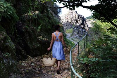 Rear view of woman holding basket while walking on mountain road