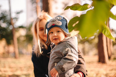 Portrait of baby boy standing by his mother in park during autum