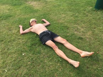 High angle view of shirtless man sleeping on grassy field while face covered with cap