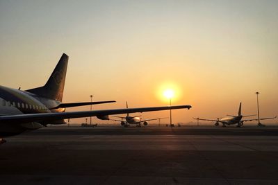 Airplane on airport runway against sky during sunset