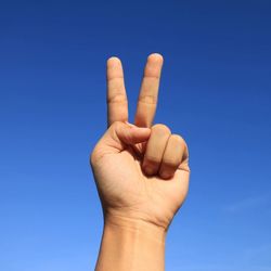 Close-up of human hand against blue sky