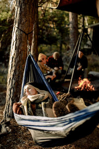 Young woman relaxing on hammock with friends camping in background