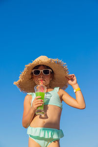 Low angle view of young woman wearing hat against clear blue sky