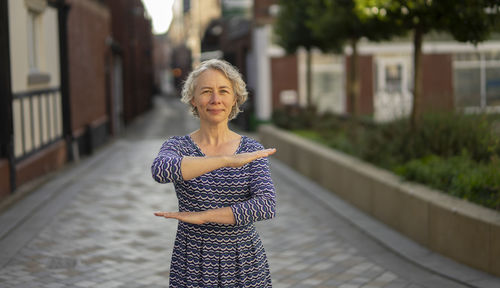 Portrait of woman gesturing while standing on footpath against buildings