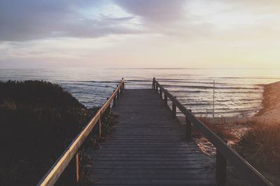 Boardwalk on sea against sky during sunset