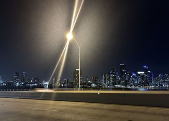 Illuminated street amidst buildings against sky at night