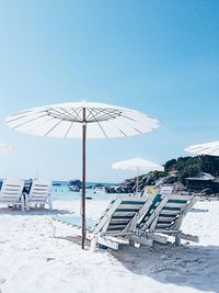 Lounge chairs with parasols at beach against clear blue sky