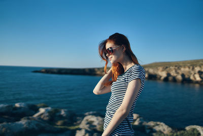 Beautiful woman standing by sea against clear blue sky