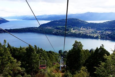 High angle view of ski lifts over forest and river against sky