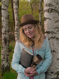 Young woman holding book by tree trunk