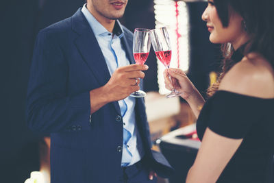 Midsection of smiling couple toasting red wineglasses while standing in bar