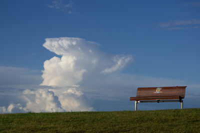 Empty bench on field against sky