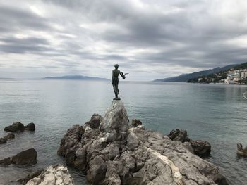 Maid standing on rock by sea against sky